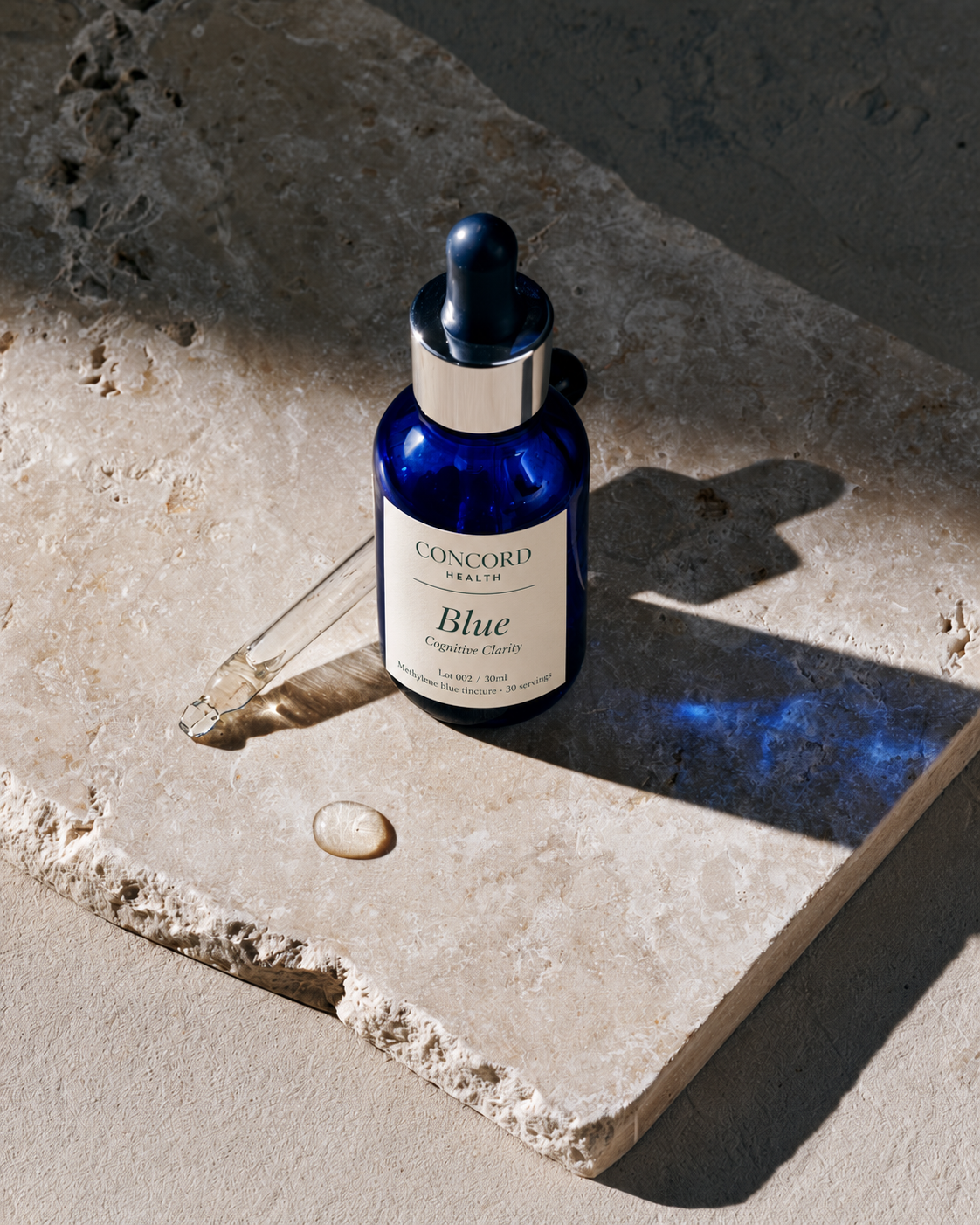 Concord Health Blue — the cobalt dropper bottle with its glass pipette set down beside a single drop of indigo on bone stone.
