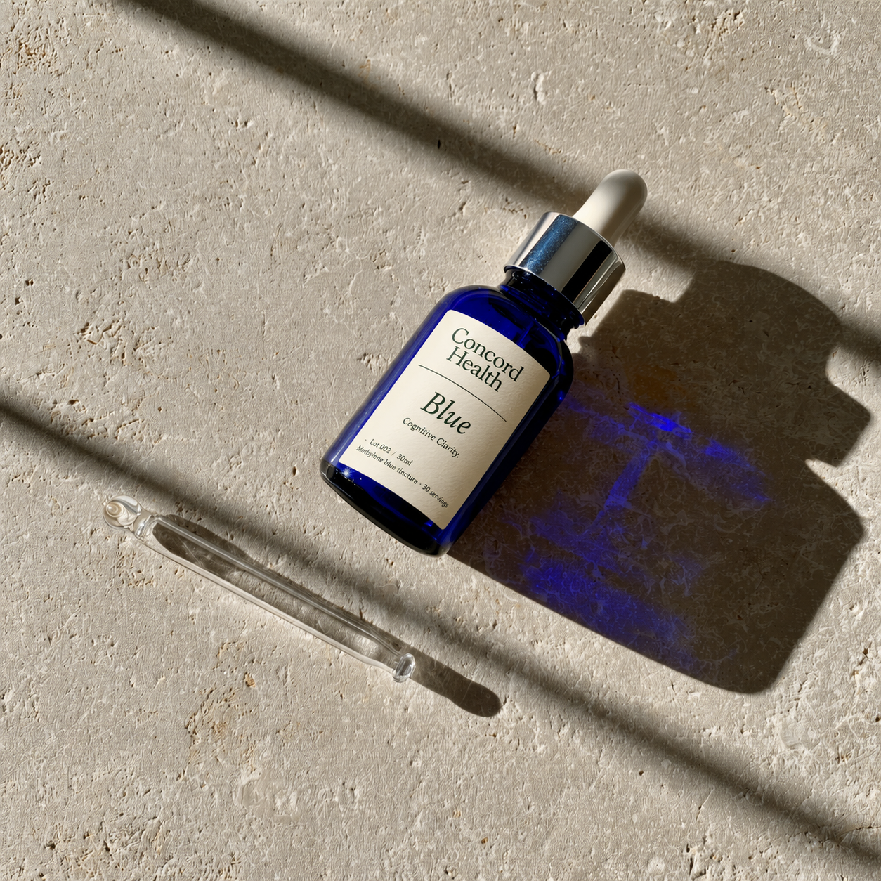 Concord Health Blue — overhead study of the cobalt dropper and its pipette in dramatic morning light.